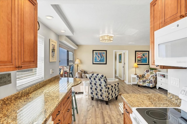 kitchen with light stone countertops, a breakfast bar, stove, and light wood-type flooring