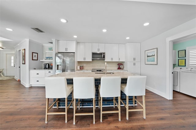 kitchen with a center island with sink, white cabinets, washing machine and dryer, a kitchen bar, and stainless steel appliances