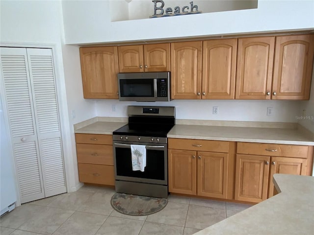 kitchen featuring light tile patterned floors, stainless steel appliances, light countertops, and brown cabinets