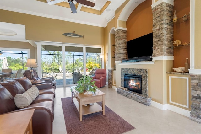 tiled living room featuring ceiling fan, a stone fireplace, ornamental molding, and a high ceiling