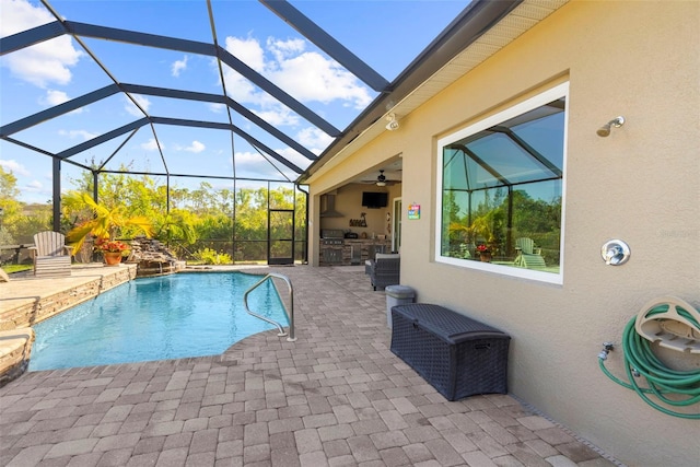 view of pool featuring pool water feature, an outdoor kitchen, a patio area, and glass enclosure