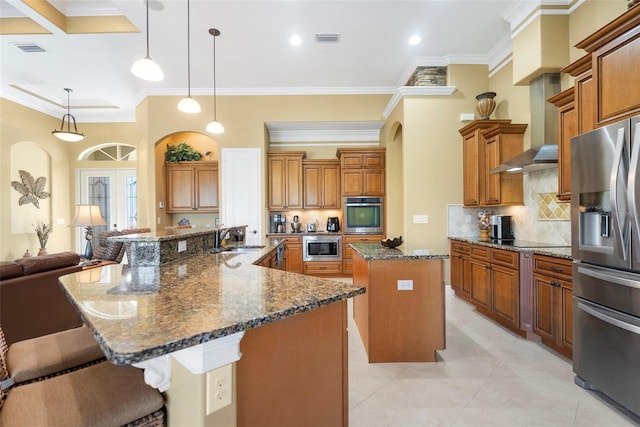 kitchen featuring wall chimney exhaust hood, stainless steel appliances, a large island with sink, crown molding, and pendant lighting