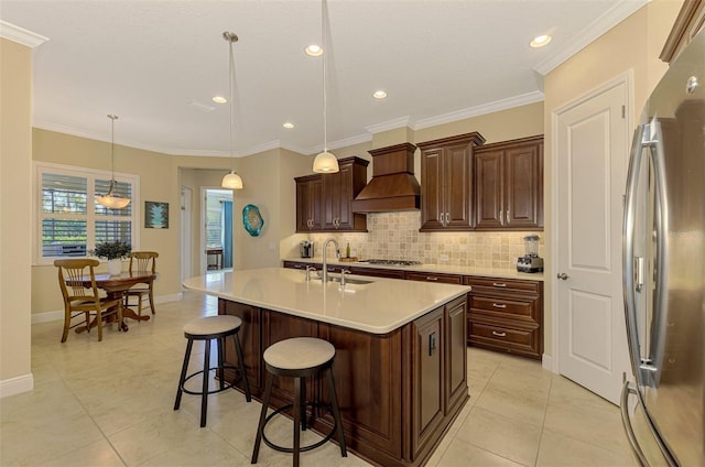 kitchen featuring pendant lighting, premium range hood, a center island with sink, crown molding, and appliances with stainless steel finishes