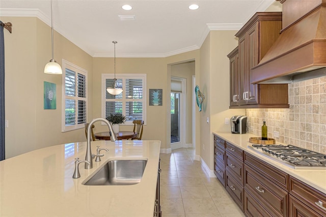 kitchen with sink, hanging light fixtures, stainless steel gas stovetop, decorative backsplash, and custom range hood