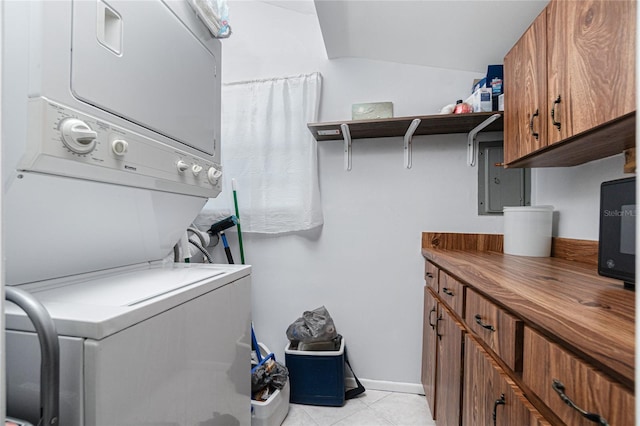 clothes washing area with light tile patterned flooring, cabinets, and stacked washing maching and dryer