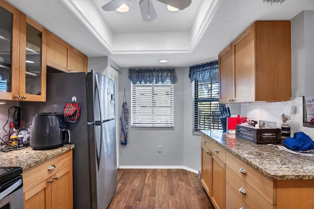 kitchen featuring light stone countertops, ceiling fan, dark wood-type flooring, stainless steel fridge, and a tray ceiling