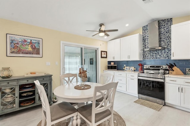 kitchen with white cabinets, wall chimney exhaust hood, lofted ceiling, and appliances with stainless steel finishes