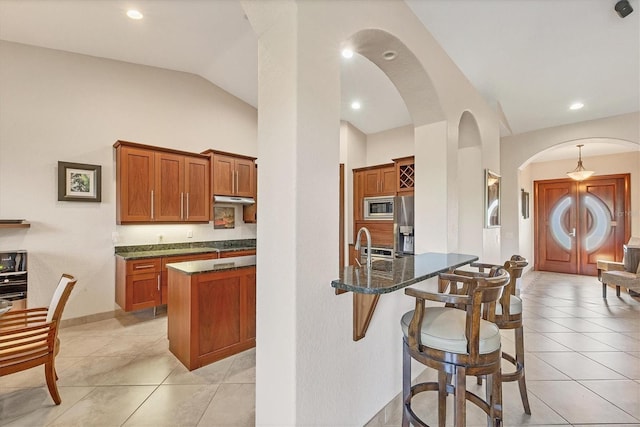 kitchen with a kitchen breakfast bar, lofted ceiling, a kitchen island with sink, light tile patterned flooring, and appliances with stainless steel finishes