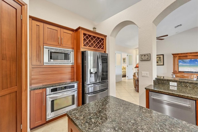 kitchen featuring ceiling fan, light tile patterned floors, appliances with stainless steel finishes, and dark stone counters