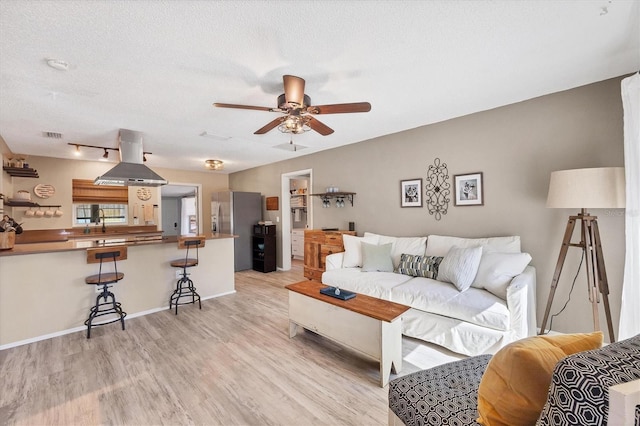 living room with ceiling fan, light hardwood / wood-style floors, and a textured ceiling