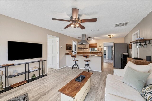 living room featuring ceiling fan, light hardwood / wood-style flooring, and a textured ceiling