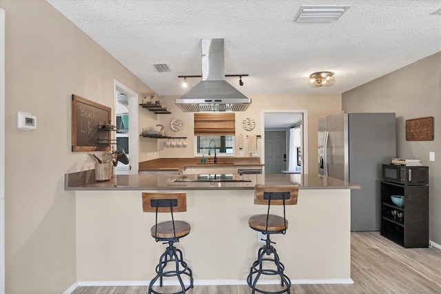 kitchen with kitchen peninsula, a kitchen bar, island range hood, and light hardwood / wood-style flooring