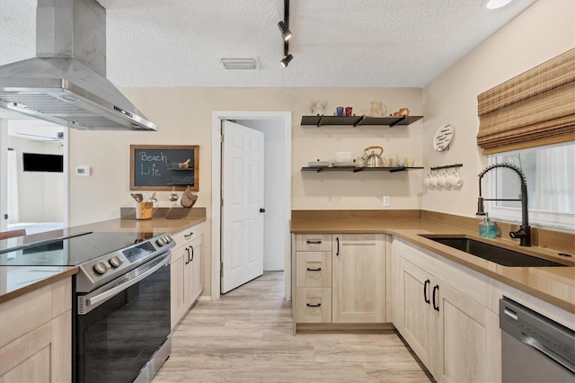 kitchen with sink, wall chimney exhaust hood, light wood-type flooring, a textured ceiling, and appliances with stainless steel finishes