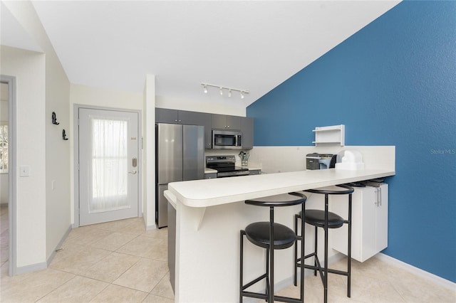 kitchen with a kitchen breakfast bar, kitchen peninsula, gray cabinetry, and appliances with stainless steel finishes