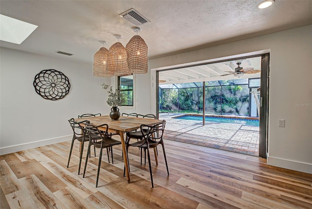 dining space with a skylight, ceiling fan, light hardwood / wood-style flooring, and a textured ceiling