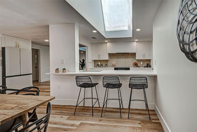 kitchen with tasteful backsplash, sink, white refrigerator, light hardwood / wood-style flooring, and white cabinets