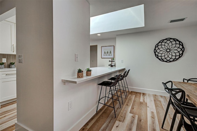 bar with light wood-type flooring, white cabinetry, and a skylight