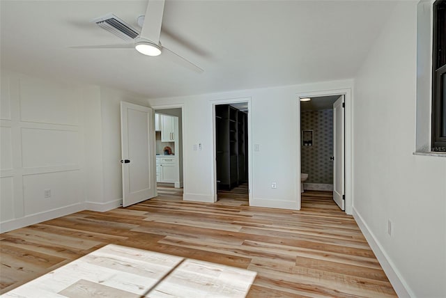 unfurnished bedroom featuring ceiling fan, a spacious closet, connected bathroom, light hardwood / wood-style floors, and a closet