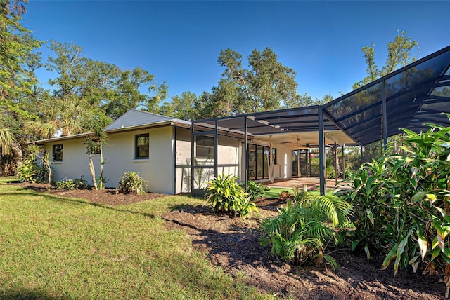 rear view of house with a patio, a yard, glass enclosure, and ceiling fan