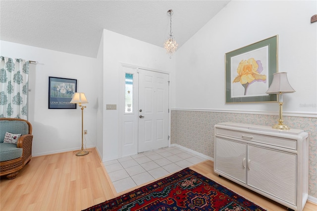 foyer featuring vaulted ceiling, light wood finished floors, a textured ceiling, and a wainscoted wall