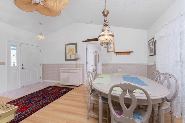 dining area featuring lofted ceiling, an inviting chandelier, light wood-style floors, wainscoting, and a textured ceiling