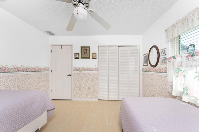 bedroom featuring a closet, visible vents, ceiling fan, a textured ceiling, and wallpapered walls