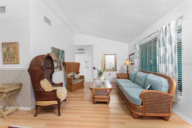 sitting room with visible vents, vaulted ceiling, light wood-style flooring, and a textured ceiling