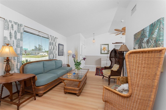 living room featuring light wood-type flooring, visible vents, vaulted ceiling, and a textured ceiling