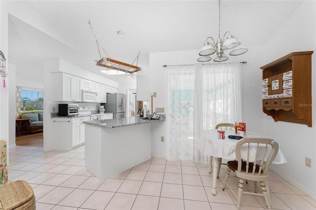 kitchen with light tile patterned floors, white microwave, white cabinets, dark stone countertops, and a peninsula