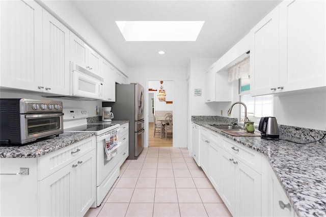 kitchen featuring light stone counters, a skylight, white cabinetry, a sink, and white appliances