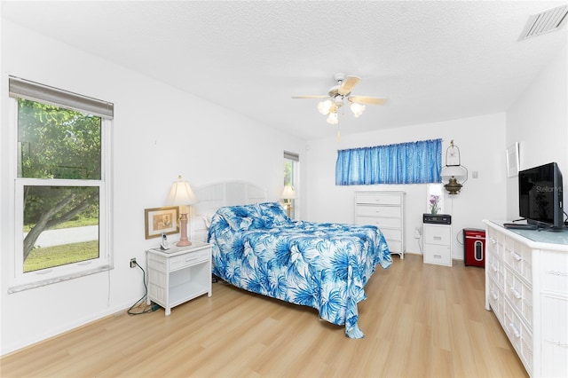 bedroom featuring light wood-type flooring, ceiling fan, visible vents, and a textured ceiling