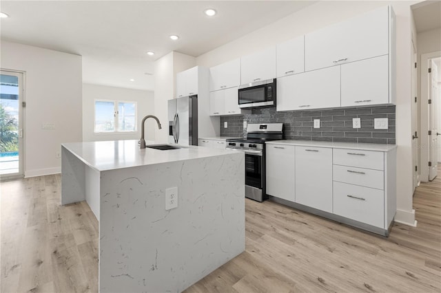 kitchen featuring white cabinetry, a center island with sink, light hardwood / wood-style floors, and appliances with stainless steel finishes