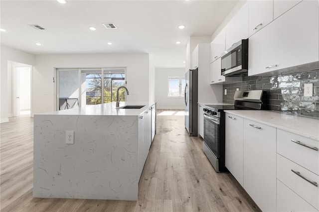 kitchen with appliances with stainless steel finishes, light wood-type flooring, a kitchen island with sink, sink, and white cabinetry