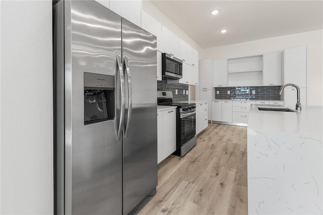 kitchen with sink, light wood-type flooring, appliances with stainless steel finishes, tasteful backsplash, and white cabinetry