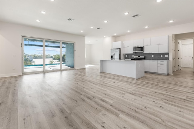 kitchen featuring white cabinets, decorative backsplash, light wood-type flooring, an island with sink, and stainless steel appliances