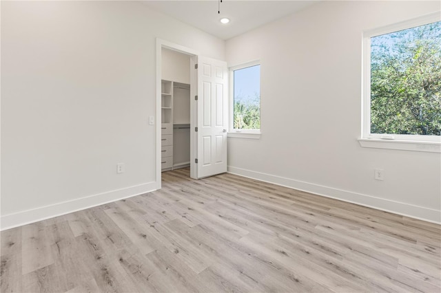 unfurnished bedroom with light hardwood / wood-style floors, a spacious closet, and a closet