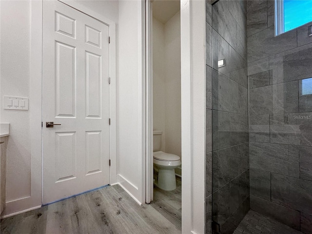 bathroom with hardwood / wood-style flooring, toilet, and tiled shower