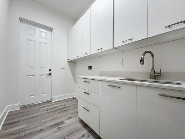 clothes washing area with washer hookup, light hardwood / wood-style floors, cabinets, and sink