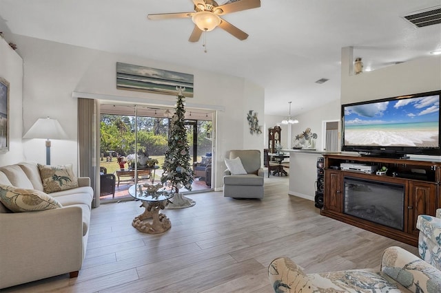 living room with lofted ceiling, light wood-type flooring, and ceiling fan with notable chandelier