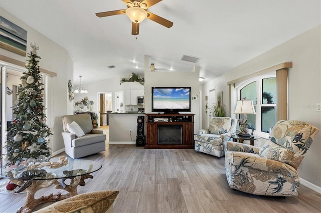 living room with light hardwood / wood-style flooring, ceiling fan with notable chandelier, and vaulted ceiling