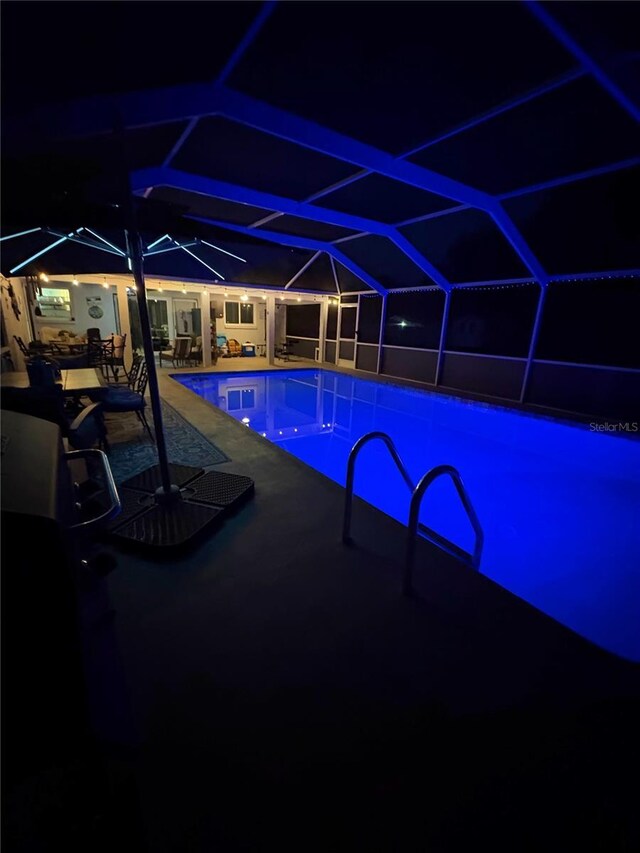 pool at night featuring a lanai and a patio area