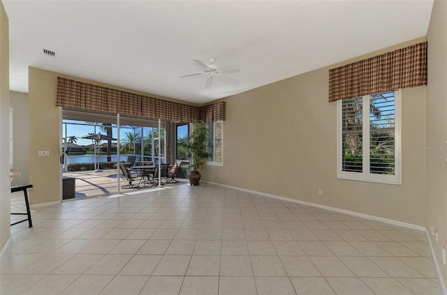 empty room featuring light tile patterned floors, a water view, plenty of natural light, and ceiling fan