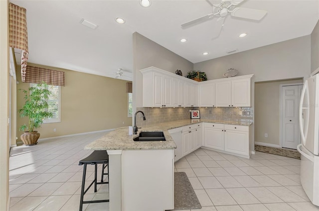 kitchen with sink, kitchen peninsula, white appliances, a breakfast bar area, and white cabinets