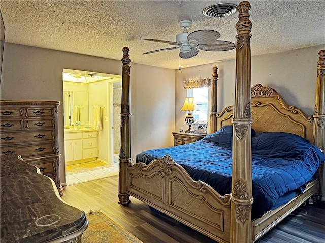 bedroom featuring a textured ceiling, hardwood / wood-style flooring, ensuite bath, and ceiling fan