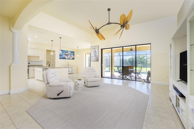 tiled living room featuring decorative columns, ceiling fan, sink, and a high ceiling