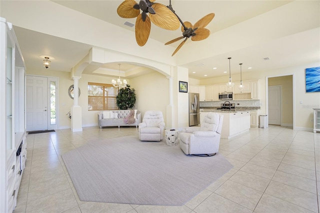 living room featuring light tile patterned floors, ceiling fan with notable chandelier, and a raised ceiling