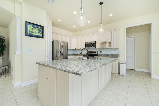 kitchen with a kitchen island with sink, light stone countertops, appliances with stainless steel finishes, tasteful backsplash, and decorative columns