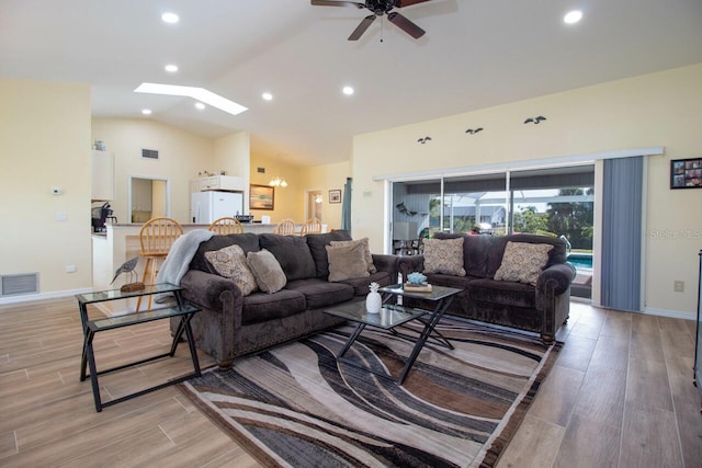 living room featuring ceiling fan, light wood-type flooring, and lofted ceiling with skylight