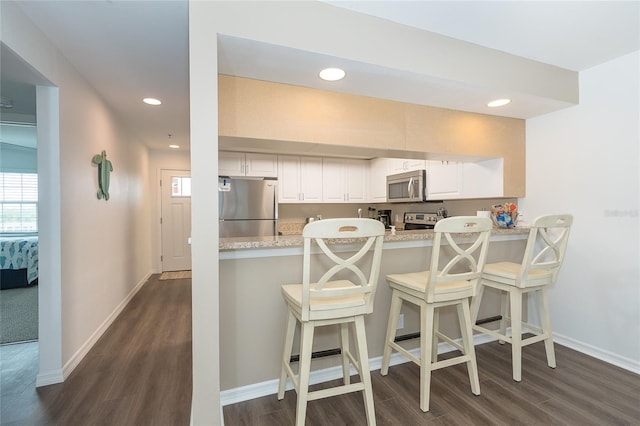 kitchen featuring a kitchen bar, appliances with stainless steel finishes, white cabinetry, and dark wood-type flooring