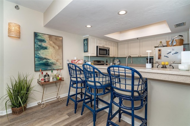 kitchen with a kitchen breakfast bar, light hardwood / wood-style floors, a raised ceiling, and white refrigerator